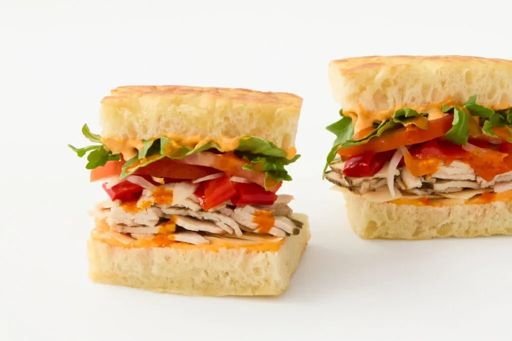 Two halves of a sandwich filled with meat, vegetables, and orange sauce.