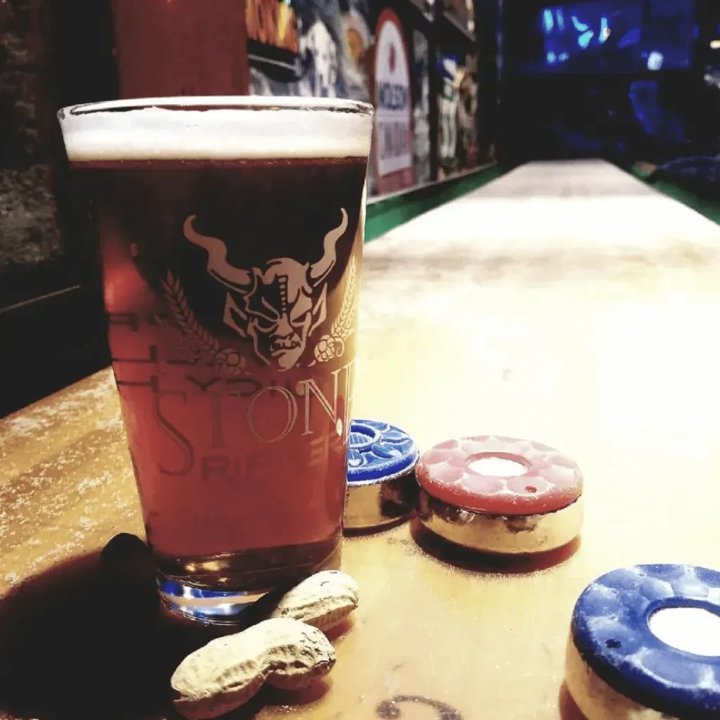 Stone beer pint, peanuts, and shuffleboard pucks on a table.