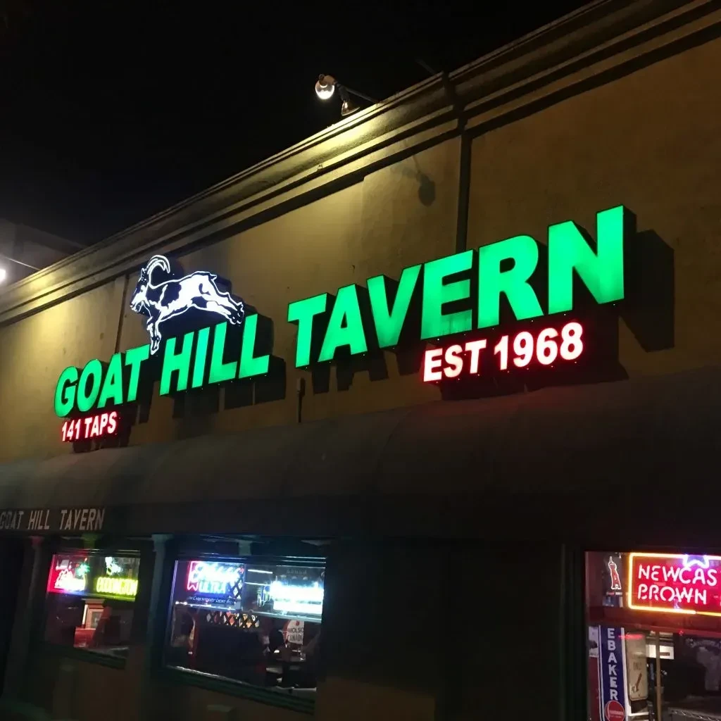 Illuminated GOAT HILL TAVERN sign with a leaping goat at night.