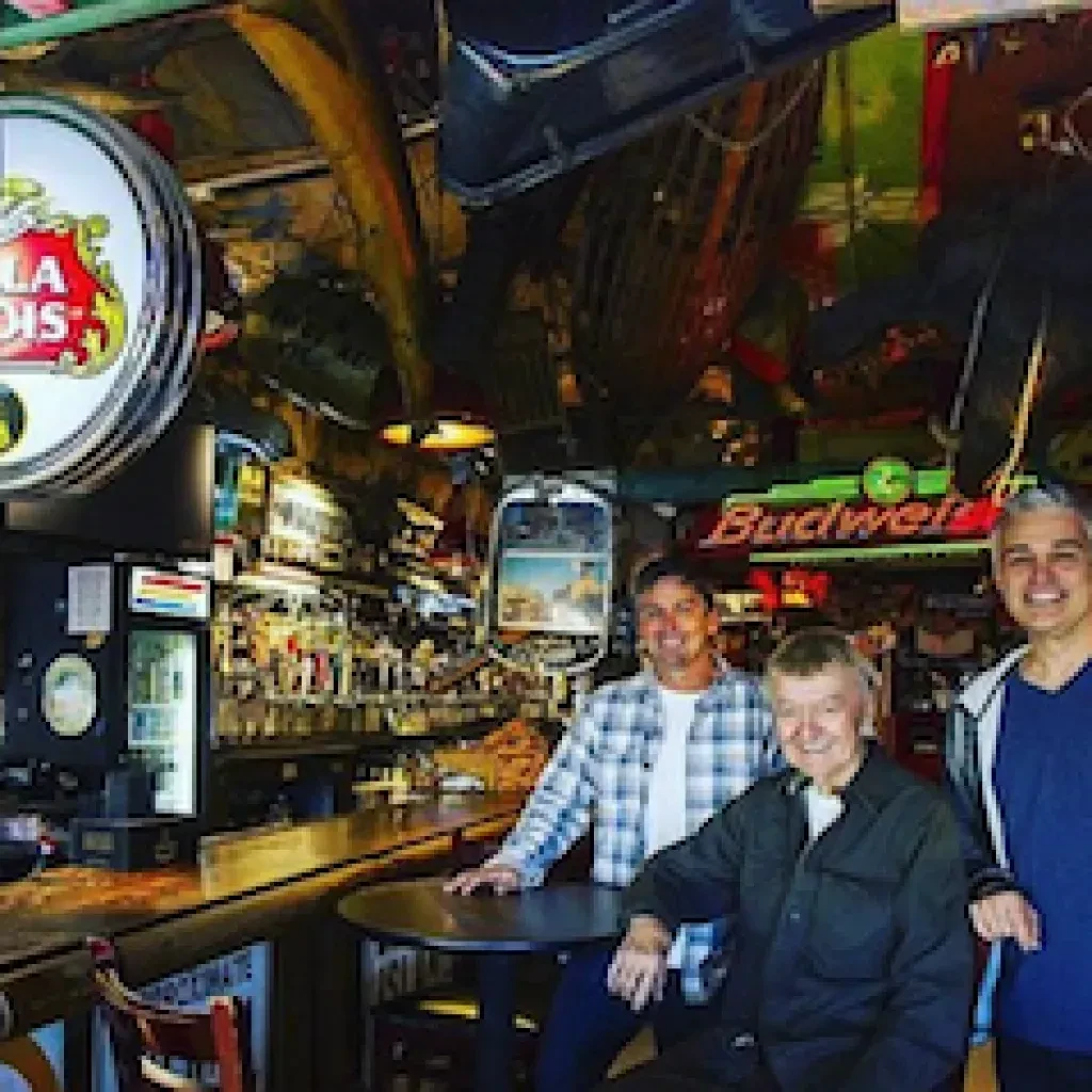 Three smiling men in a quirky bar with eclectic decorations.