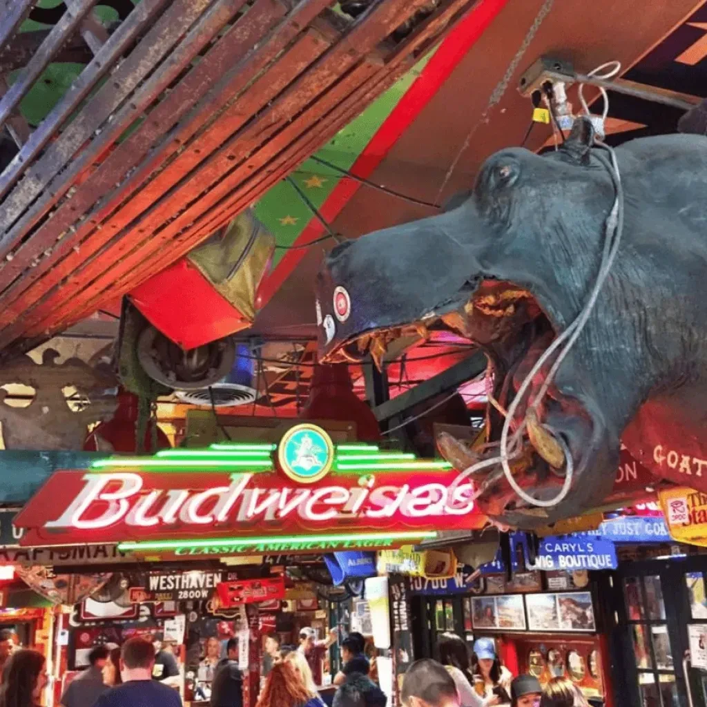 Bar interior with a hanging animal head, Budweiser neon, and many patrons.