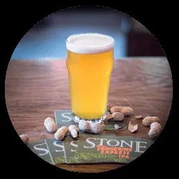 Golden beer pint with frothy head, peanuts, and Stone IPA coasters.