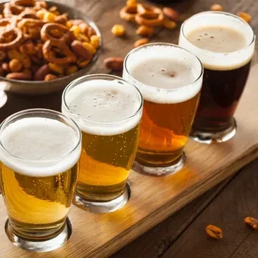 Four different beers in tasting glasses on a wooden paddle with snacks.