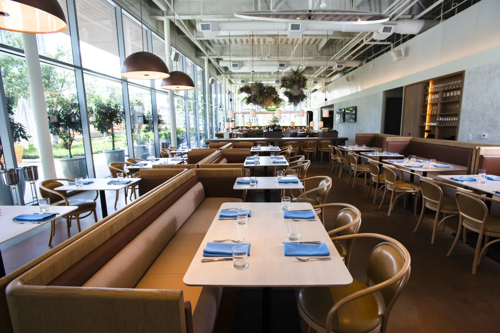 Modern, well-lit restaurant interior with booths, tables, a bar, and large windows.