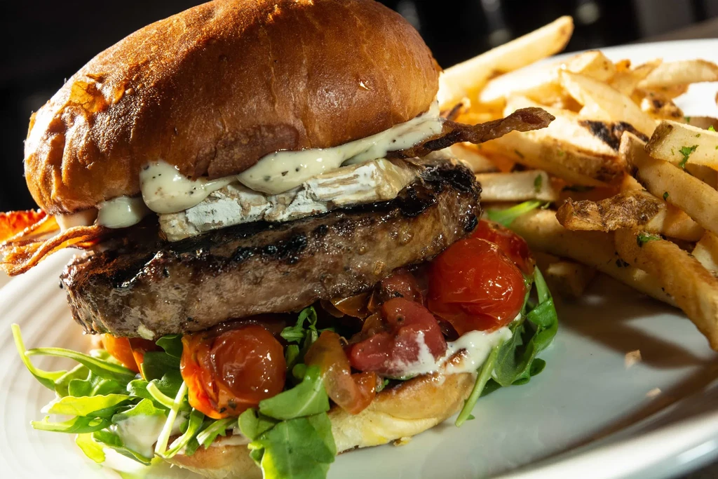 Gourmet burger with melted cheese, bacon, arugula, and seasoned fries.