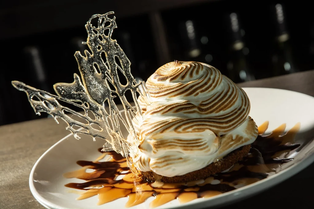 Artfully presented toasted meringue dessert with sauces and sugar decoration.