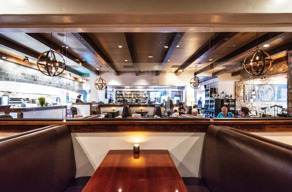 Warm, sophisticated restaurant interior with open kitchen, bar, and booths.