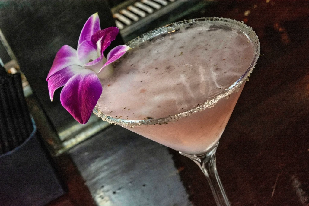 Martini glass with a pink frothy cocktail, sparkling rim, and orchid.