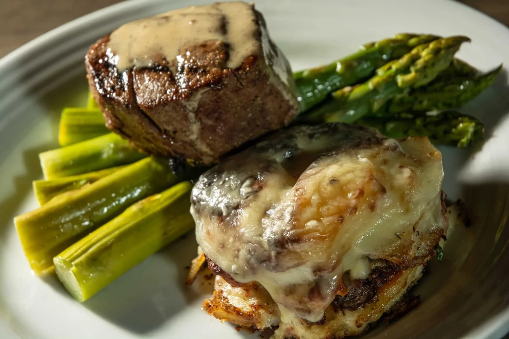 Plated gourmet meal: seared meat, cheesy gratin, green asparagus.