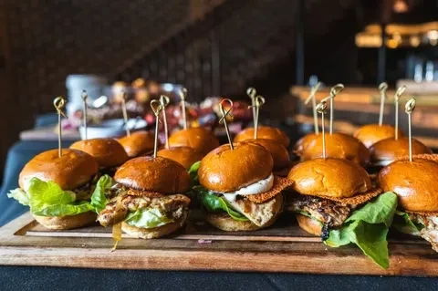 Platter of gourmet sliders with lettuce, patty, and sauce on a wooden board.