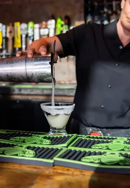 Bartender pouring frothy drink from shaker into salt-rimmed margarita glass.