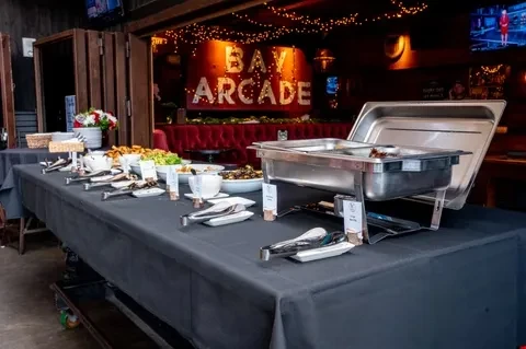 Buffet table with diverse food, chafing dishes, and "BAY ARCADE" sign.