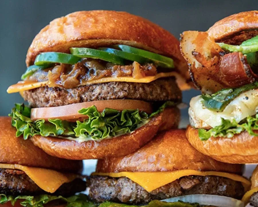Arrangement of gourmet burgers with cheese, lettuce, tomato, bacon, and jalapeños.