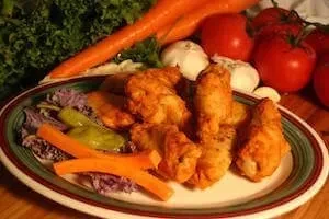 Plate of orange-red chicken wings, carrots, and pickled peppers on greens.