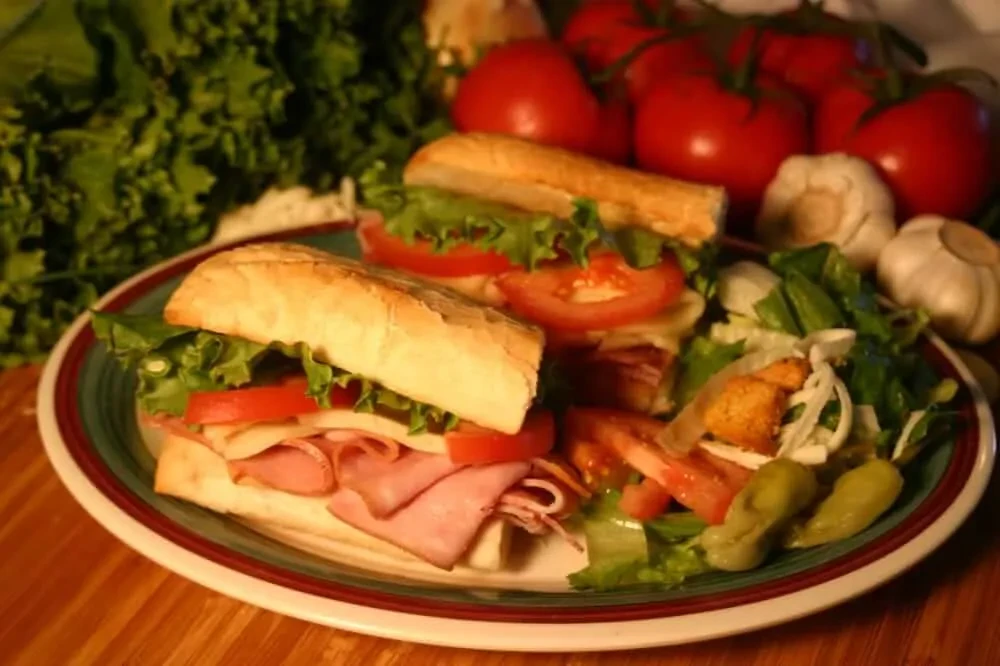 Two deli sub sandwiches, a fresh salad, and raw ingredients.
