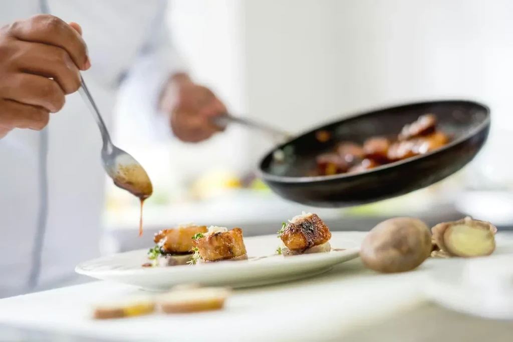 Chef drizzles sauce onto precisely plated seared food.
