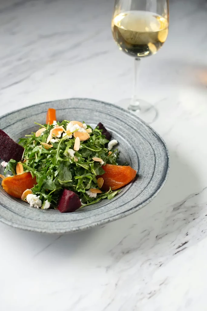 Arugula salad with cheese, beetroot, almonds, and white wine on marble.