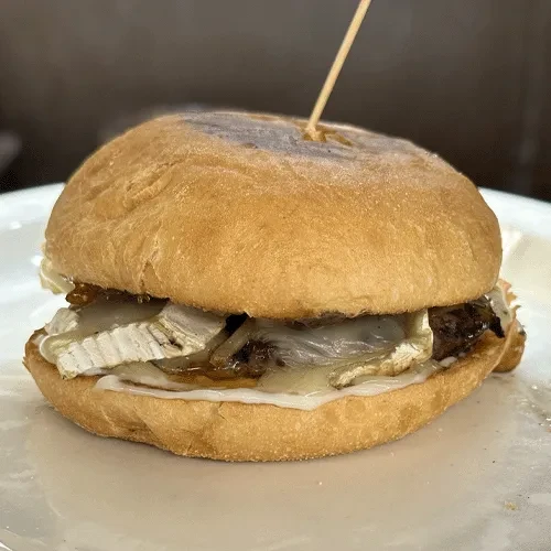 Gourmet sandwich with brie, caramelized onions, patty on white plate.