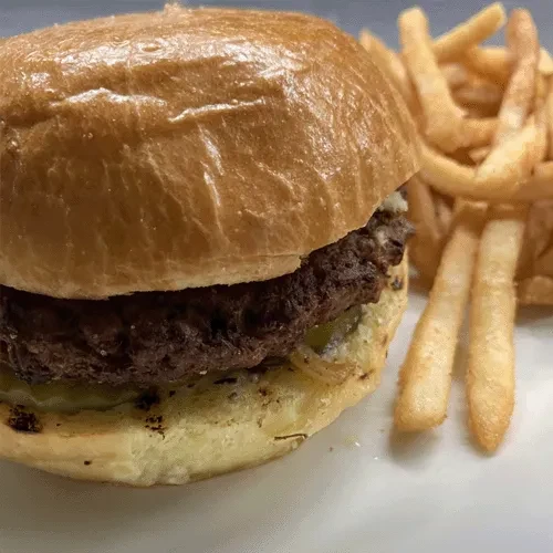 Close-up hamburger, pickles, and golden french fries on a white surface.