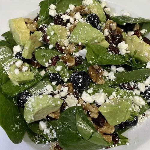Close-up salad with spinach, avocado, feta, walnuts, cranberries, blueberries.