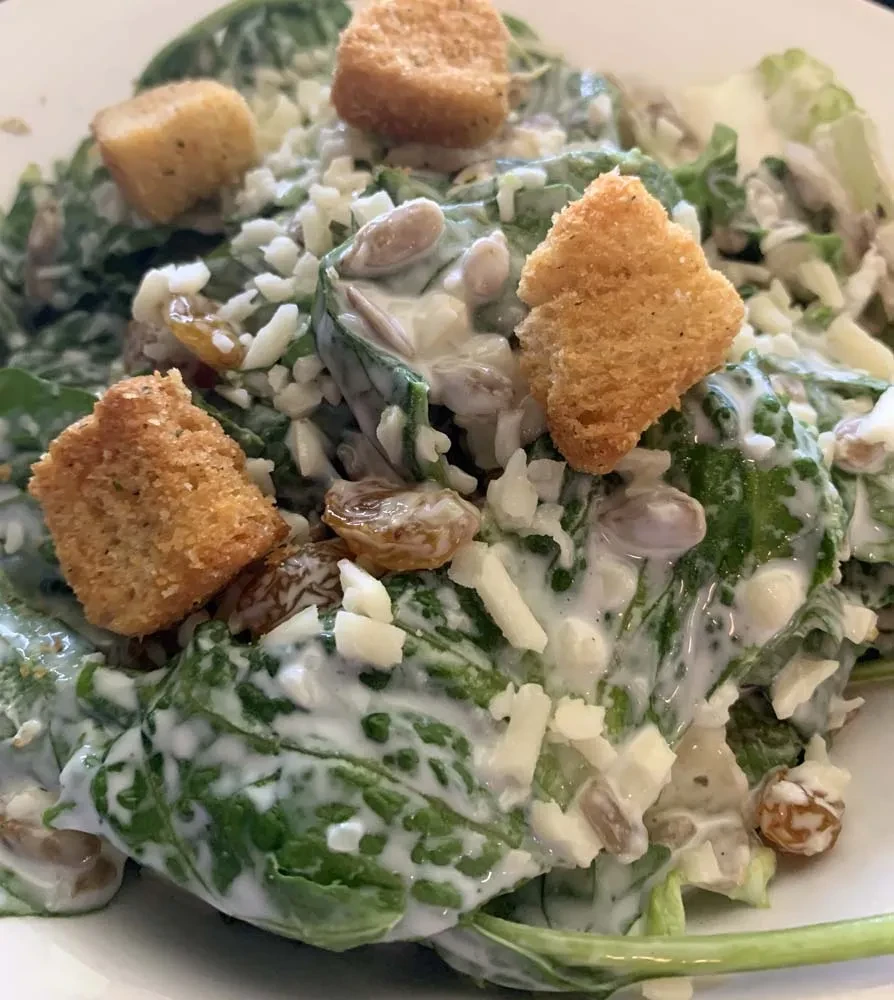 Close-up fresh green salad with creamy dressing, croutons, cheese, raisins, seeds.