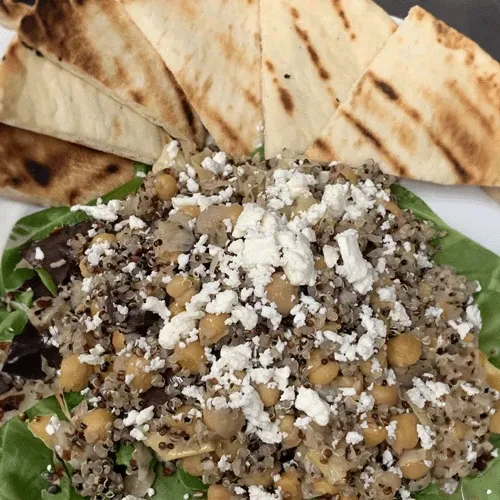 Plate of spinach, chickpea, and quinoa salad with feta and pita.