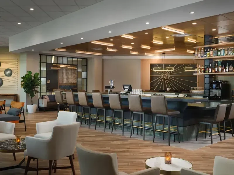 Modern bar and lounge with white seating, dark counter, and sunburst art.