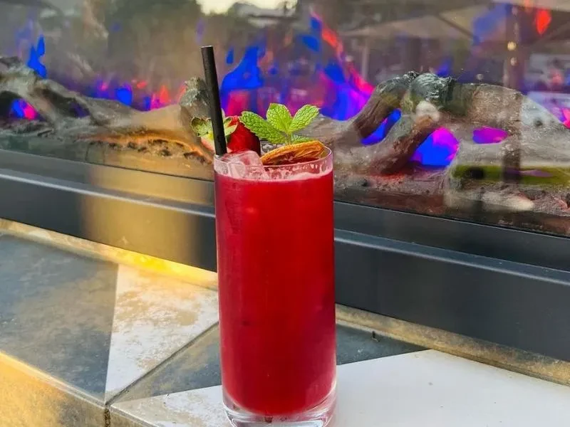 Vibrant red drink with garnishes by an LED fireplace.