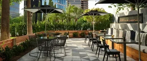 Empty modern urban patio with tables, built-in bench, fireplace, string lights.