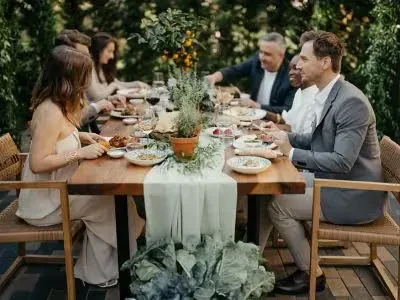 Six people dining at a long wooden table in a lush garden.