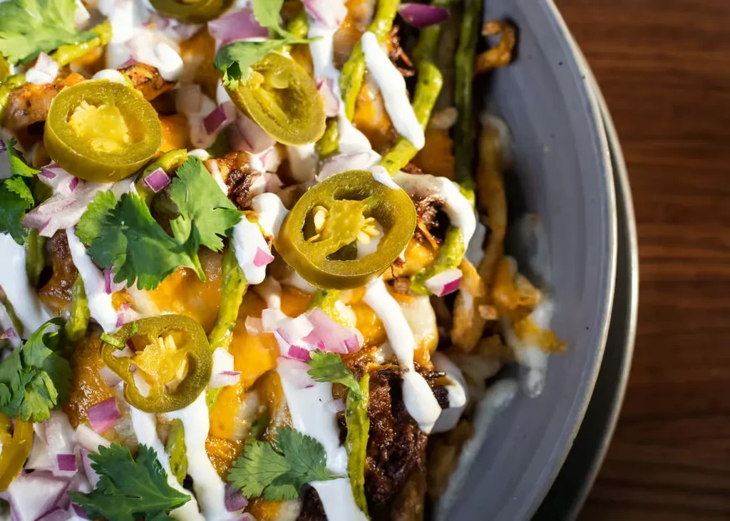 Bowl of loaded fries or nachos with cheese, jalapeños, and cilantro.