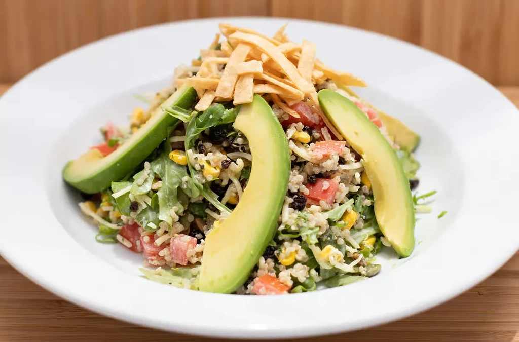 Colorful grain salad with quinoa, avocado, corn, and crispy strips.
