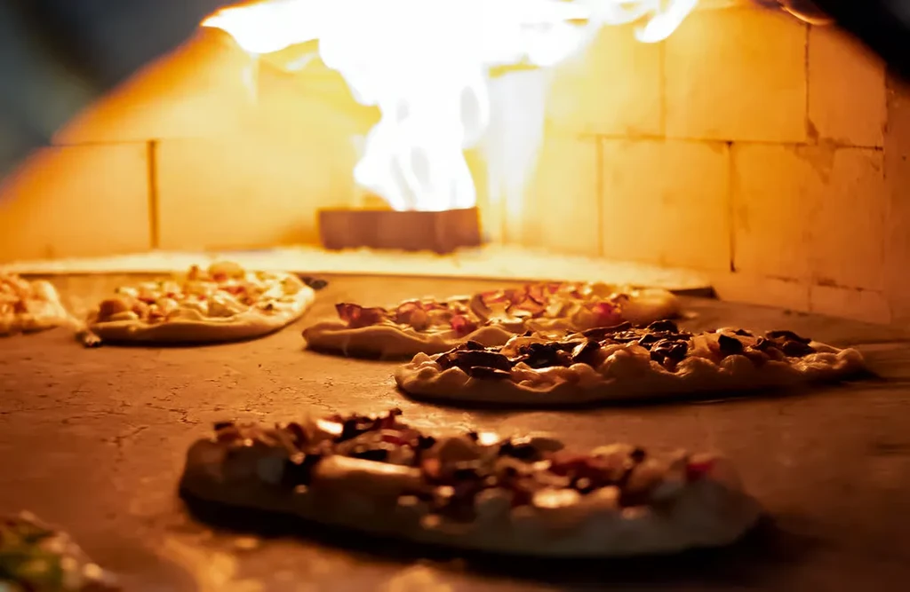 Pizzas baking inside a brick wood-fired oven with flames.