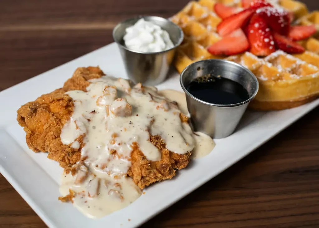 Fried chicken and waffle with strawberries, gravy, whipped cream, and syrup.