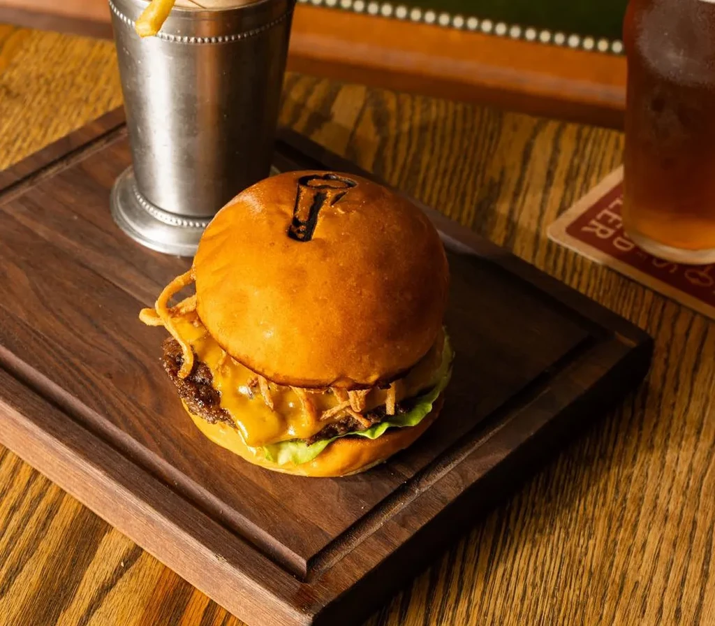 Gourmet hamburger on a wooden board with fries and beer.