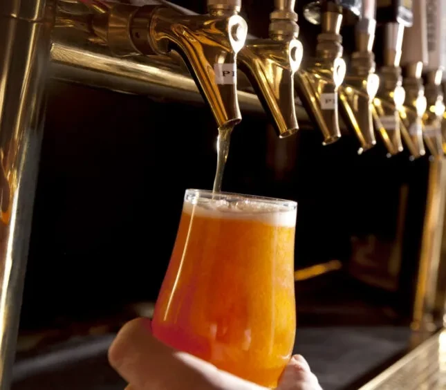 Golden tap pours frothy amber beer into a glass held by hand.