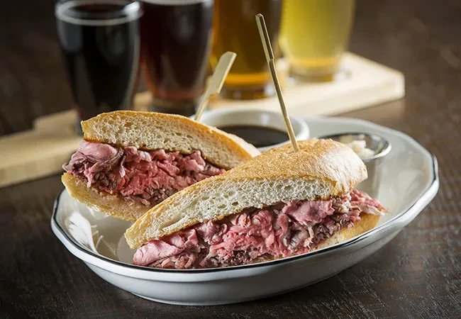 Roast beef sandwich halves, dipping sauce, white condiment, and background beers.