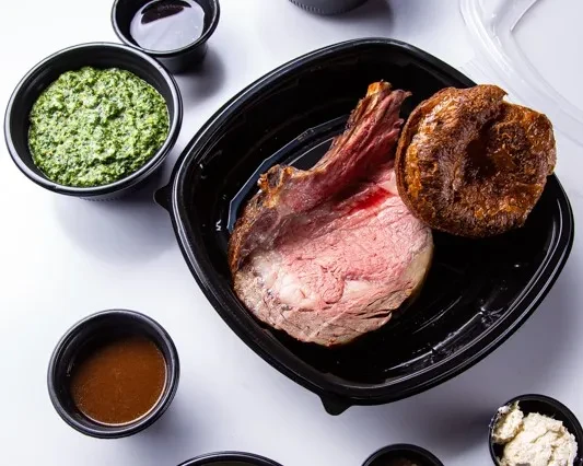 Overhead takeout meal with sliced roast beef, Yorkshire pudding, and sauces.