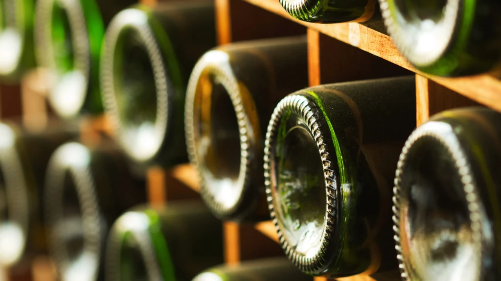 Textured dark green wine bottle bottoms in focus, stored in wooden racks.