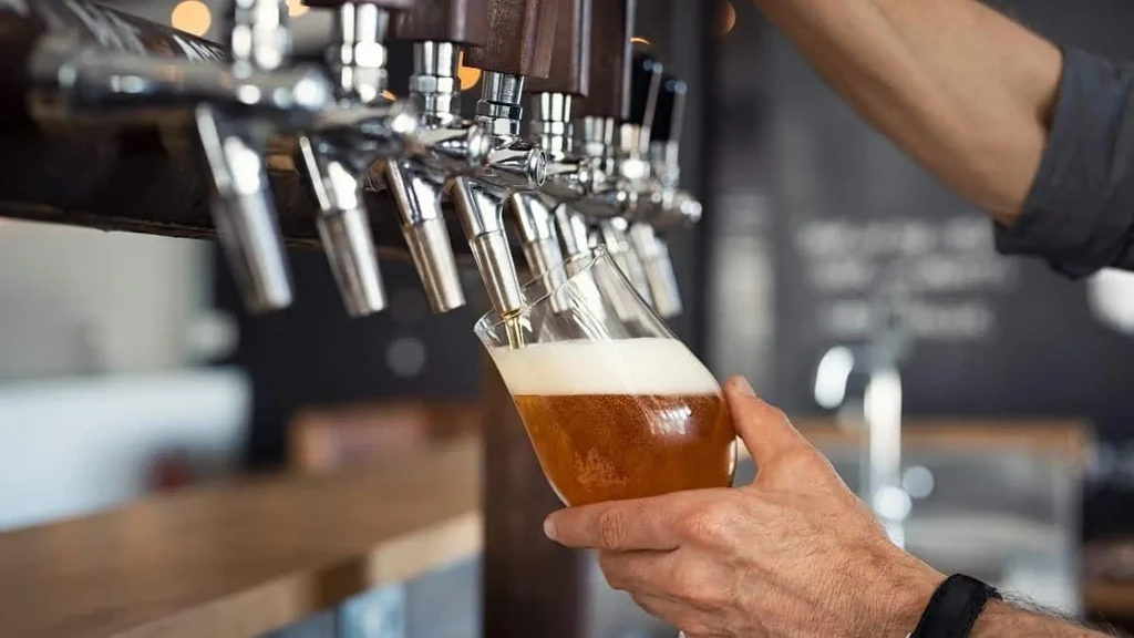 Close-up of hand filling glass with golden beer from a tap.