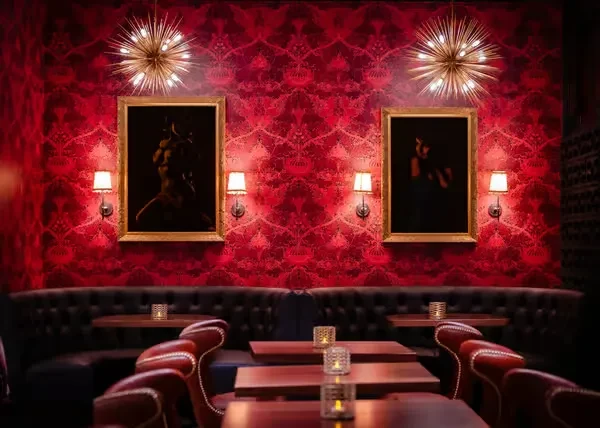 Red damask restaurant interior with chandeliers and classical nude paintings.