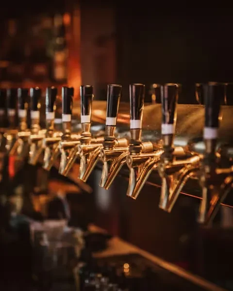 Seven golden beer taps with dark handles in a dim bar.