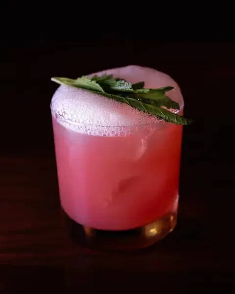 Pink cocktail with frothy foam, ice, and fresh mint.