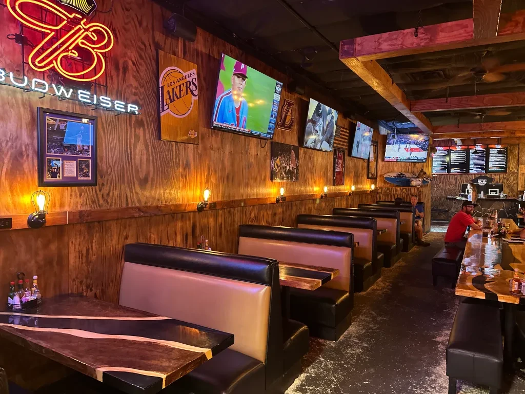 Dimly lit rustic sports bar with wood walls, Budweiser sign, and TVs.