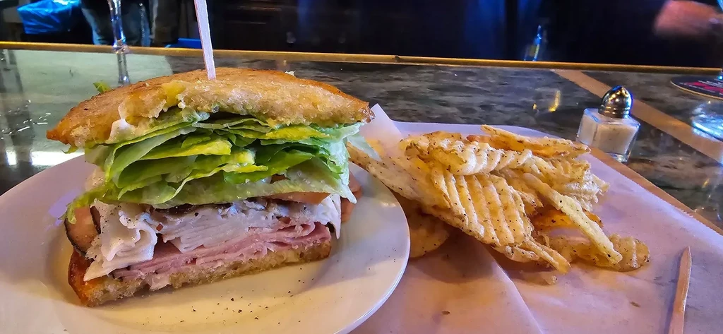 Stacked deli sandwich and seasoned waffle chips on a dark counter.