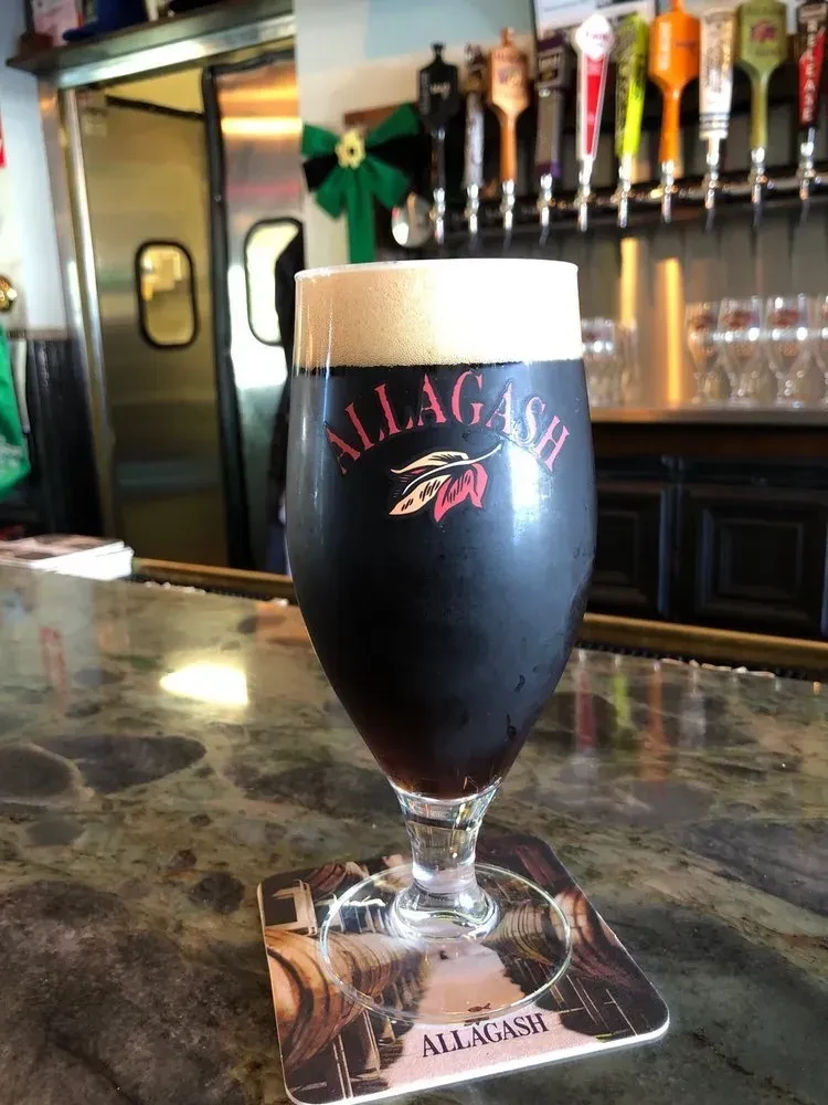 Dark Allagash beer in a tulip glass on a bar with taps.