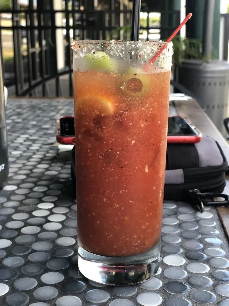 Bloody Mary with salt rim, lime, straw on gray tiled table.