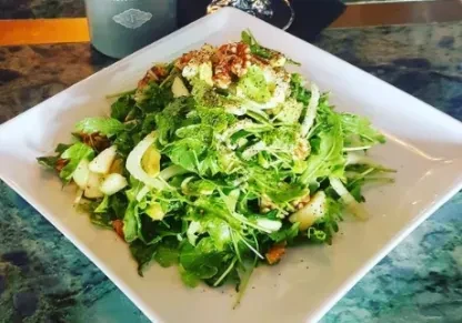 Fresh green salad with walnuts and sliced ingredients on a white plate.