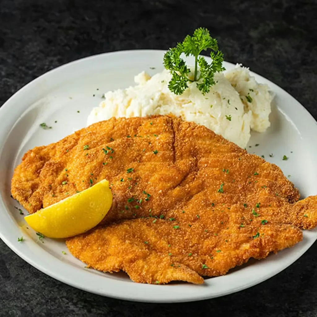 Golden-brown schnitzel or fish, mashed potatoes, and lemon on a plate.