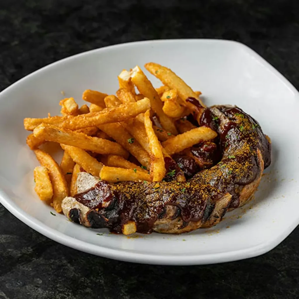 Grilled sausage, dark sauce, French fries, and herbs on white plate.